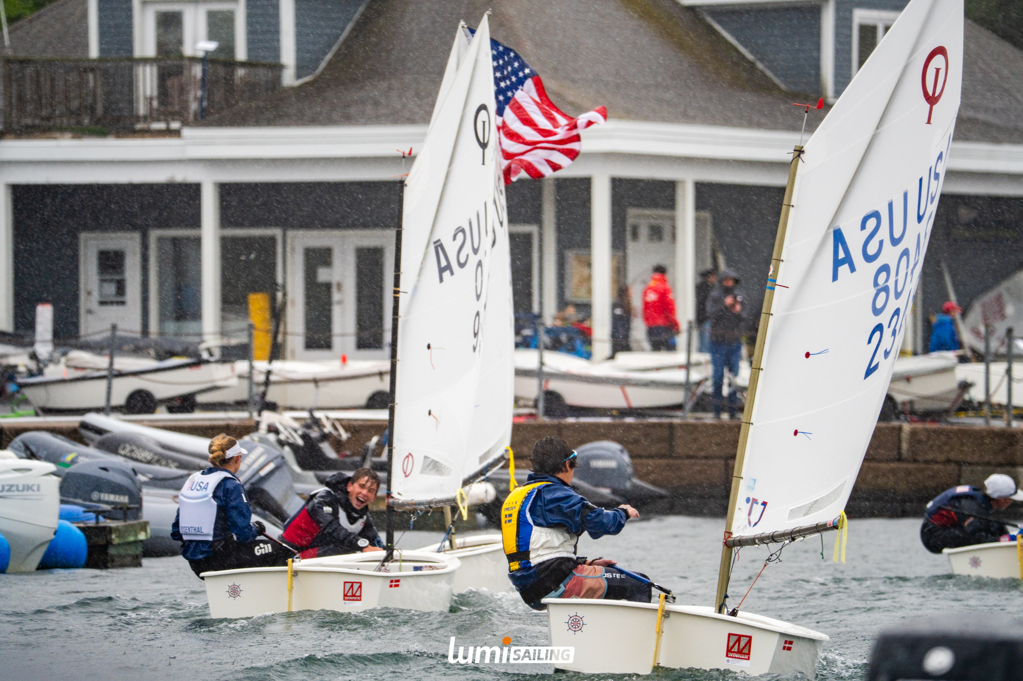 Optimist sailors racing in heavy rain near shore